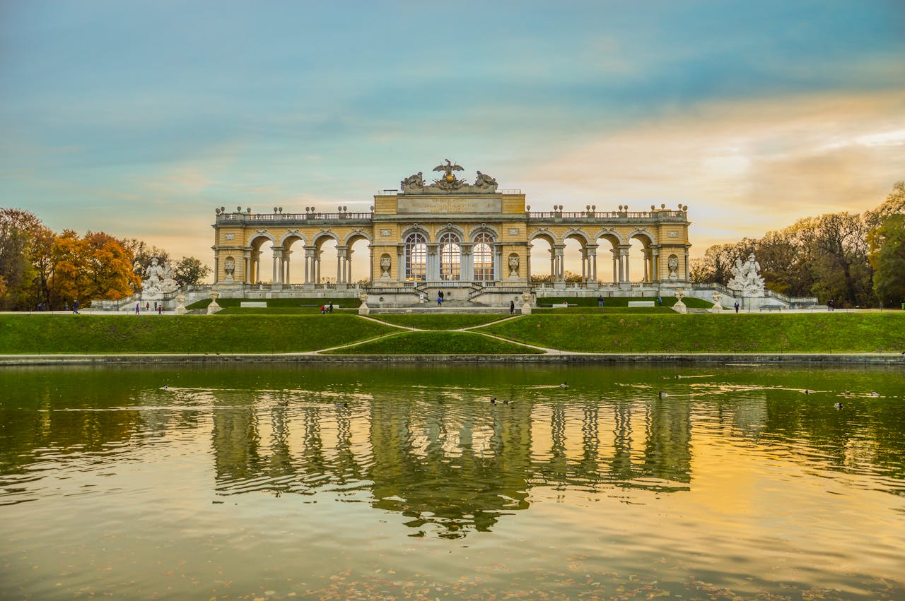 services-bg A stunning view of Schönbrunn Palace's Gloriette reflecting in a tranquil pond at sunset.